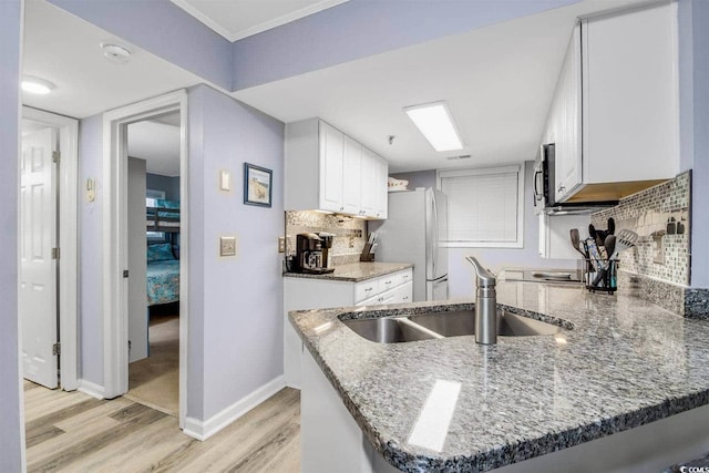 kitchen featuring backsplash, light stone counters, light wood-style floors, stainless steel appliances, and a sink