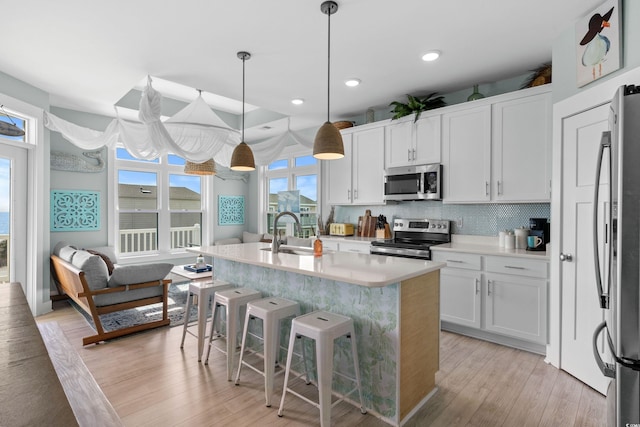 kitchen with light wood-style flooring, a center island with sink, a sink, stainless steel appliances, and light countertops