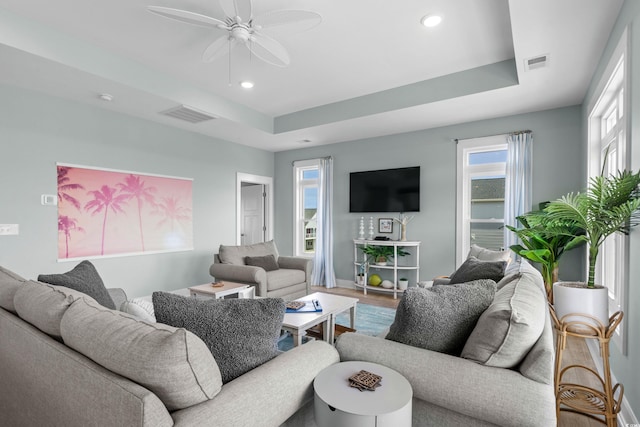 living room with a raised ceiling, recessed lighting, visible vents, and ceiling fan