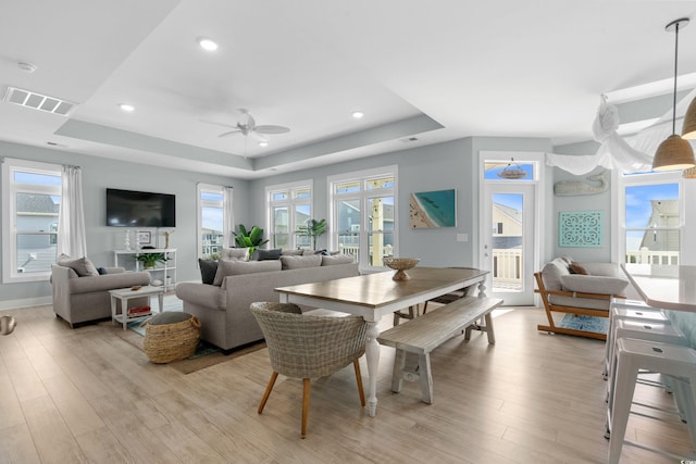 dining room with visible vents, a raised ceiling, a healthy amount of sunlight, and light wood-style flooring