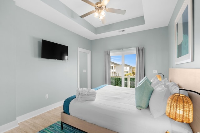 bedroom featuring a ceiling fan, wood finished floors, baseboards, visible vents, and a raised ceiling