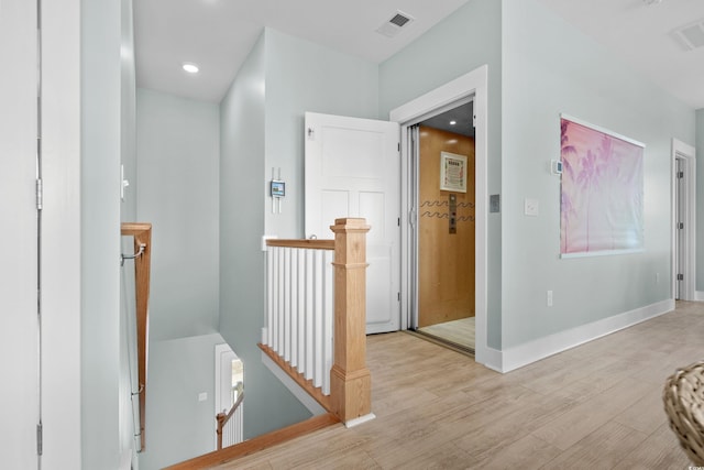 hall with an upstairs landing, visible vents, light wood-style flooring, and baseboards