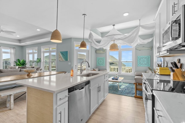 kitchen with a sink, light countertops, light wood-style floors, appliances with stainless steel finishes, and open floor plan