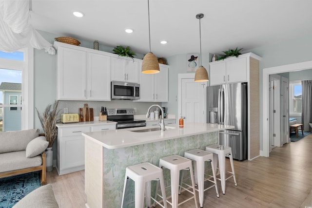 kitchen with a sink, stainless steel appliances, light countertops, a kitchen bar, and light wood-type flooring