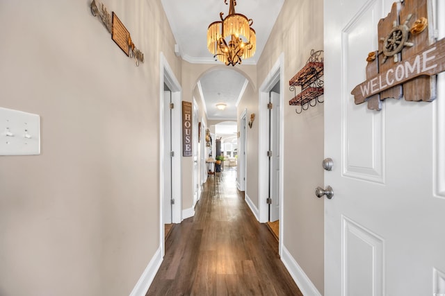 corridor featuring arched walkways, dark wood finished floors, crown molding, a chandelier, and baseboards