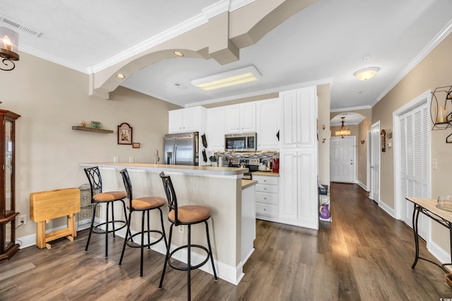 kitchen featuring arched walkways, stainless steel appliances, a breakfast bar area, and white cabinets