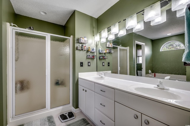 bathroom featuring a textured ceiling, double vanity, a sink, and a shower stall