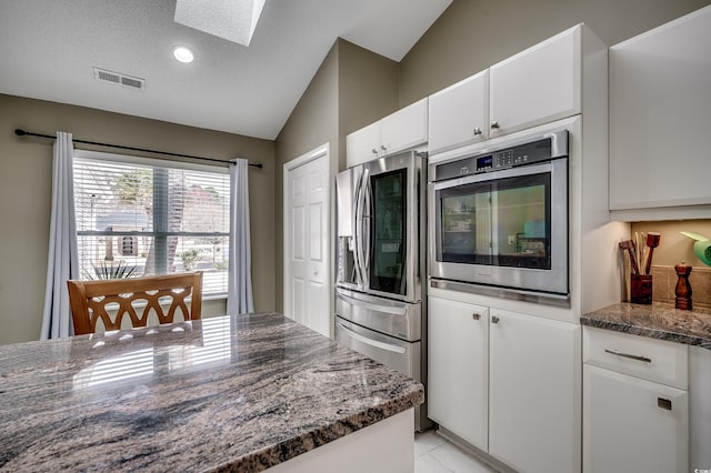 kitchen featuring visible vents, appliances with stainless steel finishes, white cabinets, dark stone counters, and vaulted ceiling with skylight