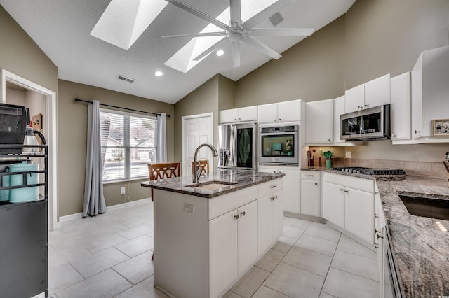 kitchen with stainless steel appliances, visible vents, a kitchen island with sink, a sink, and dark stone countertops