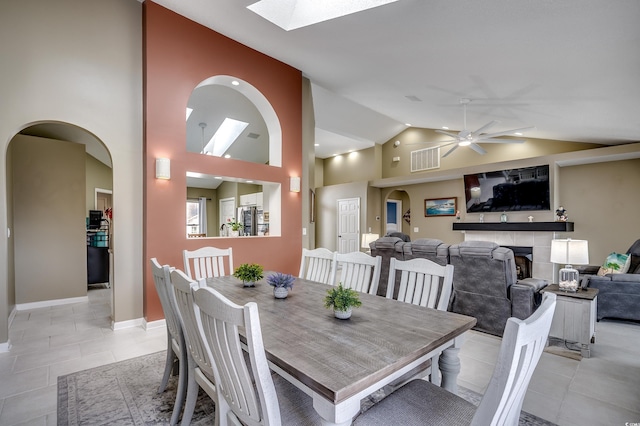 dining area featuring light tile patterned floors, visible vents, arched walkways, a tile fireplace, and ceiling fan