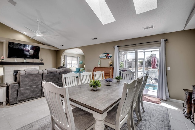 dining space with lofted ceiling with skylight, light tile patterned floors, visible vents, and arched walkways