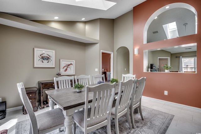 dining space with a skylight, light tile patterned floors, recessed lighting, high vaulted ceiling, and baseboards