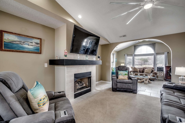 living area with arched walkways, visible vents, light carpet, vaulted ceiling, and a tile fireplace