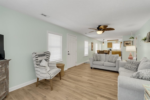 living area featuring baseboards, visible vents, light wood finished floors, and ceiling fan