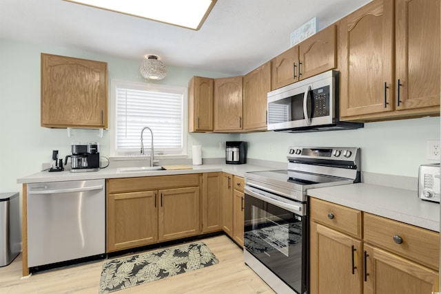 kitchen with a sink, stainless steel appliances, light wood-type flooring, and light countertops