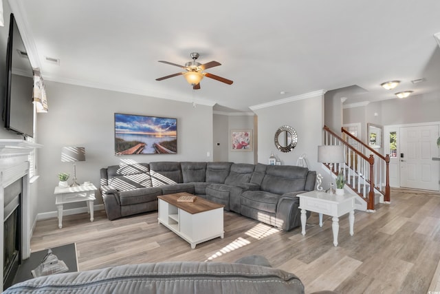 living room with light wood-style floors, stairs, ornamental molding, and a fireplace