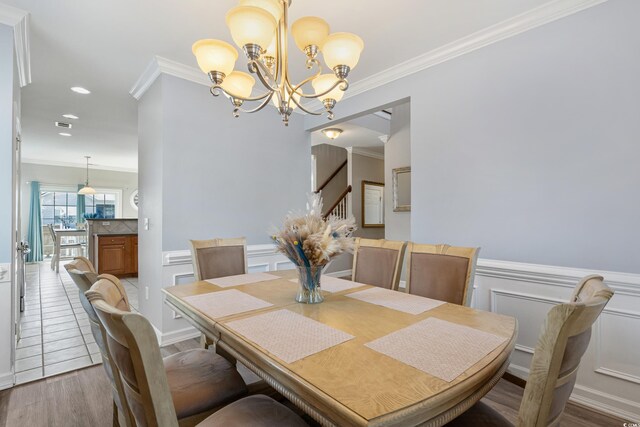 dining space featuring a wainscoted wall, stairway, ornamental molding, wood finished floors, and a chandelier