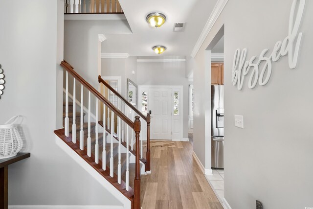 entrance foyer with ornamental molding, visible vents, light wood-style flooring, and stairs