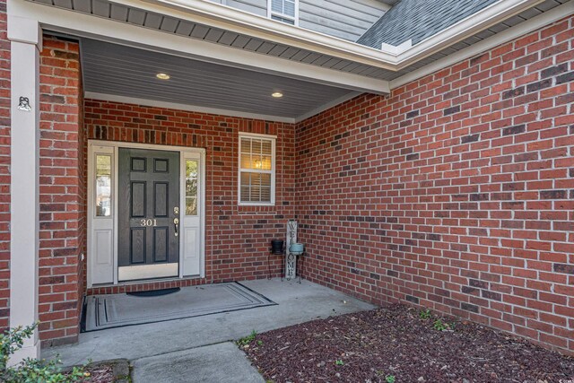 entrance to property featuring brick siding and roof with shingles