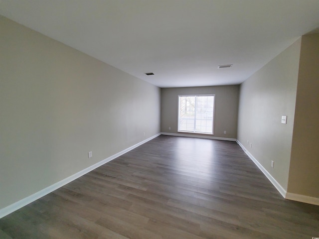 unfurnished room with dark wood-style floors, visible vents, and baseboards