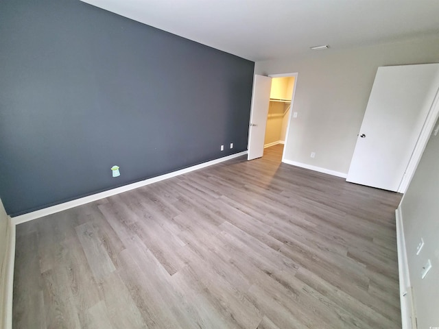 unfurnished bedroom with a closet, a spacious closet, baseboards, and wood finished floors