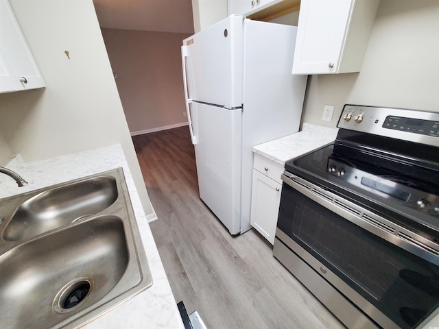 kitchen featuring white cabinets, freestanding refrigerator, light wood-type flooring, stainless steel range with electric stovetop, and a sink