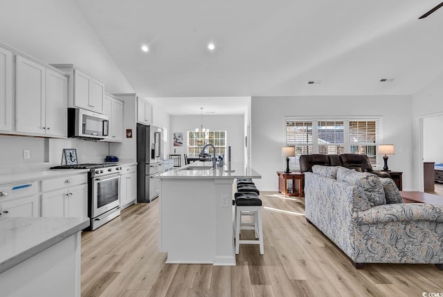 kitchen featuring open floor plan, stainless steel appliances, light wood-type flooring, a chandelier, and a sink