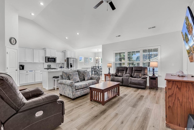 living room with ceiling fan with notable chandelier, high vaulted ceiling, light wood finished floors, and visible vents