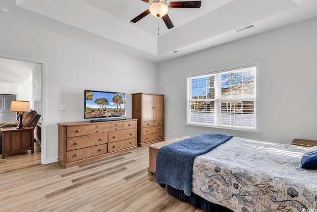 bedroom featuring light wood finished floors, a raised ceiling, visible vents, ceiling fan, and baseboards