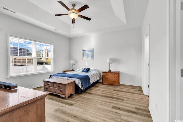 bedroom featuring ceiling fan, visible vents, baseboards, light wood-style floors, and a tray ceiling