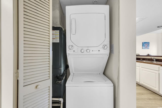 washroom featuring laundry area, light wood-style flooring, stacked washer / drying machine, and a sink