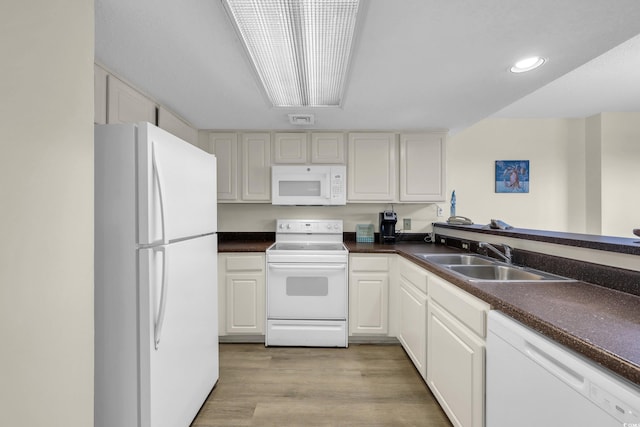 kitchen with dark countertops, light wood-type flooring, white cabinets, white appliances, and a sink