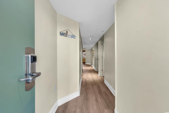 hall featuring baseboards, a textured ceiling, and wood finished floors