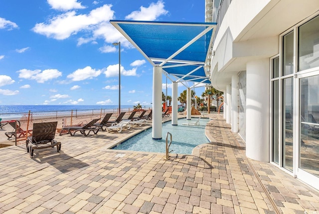 community pool with a lanai, a water view, a view of the beach, and a patio