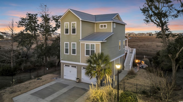 view of front of property featuring concrete driveway, metal roof, fence, a garage, and stairs