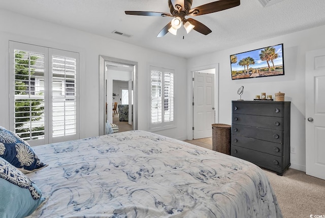 bedroom with a textured ceiling, a ceiling fan, visible vents, and light colored carpet