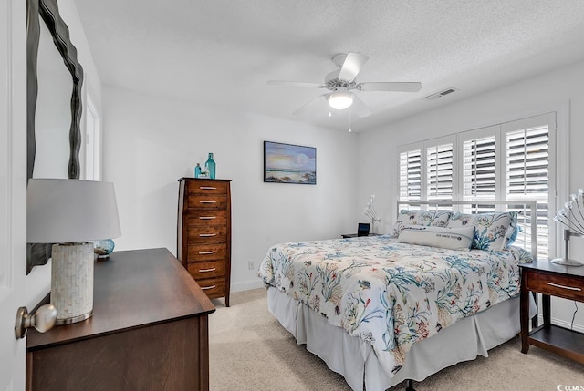 bedroom featuring a textured ceiling, ceiling fan, light colored carpet, visible vents, and baseboards