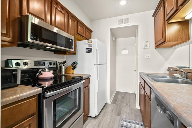 kitchen featuring visible vents, light wood finished floors, a sink, stainless steel appliances, and brown cabinets