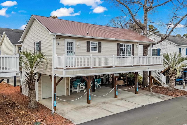 rear view of house with an attached garage, driveway, stairway, and metal roof