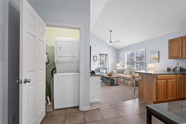 laundry area featuring carpet floors, stacked washer and dryer, a ceiling fan, tile patterned flooring, and laundry area