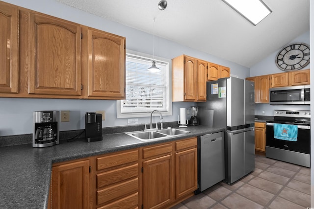 kitchen with a sink, hanging light fixtures, appliances with stainless steel finishes, brown cabinetry, and dark countertops