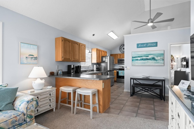 kitchen featuring lofted ceiling, a peninsula, a sink, appliances with stainless steel finishes, and brown cabinets