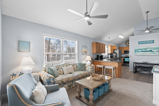 living room with ceiling fan, light tile patterned flooring, light carpet, baseboards, and vaulted ceiling