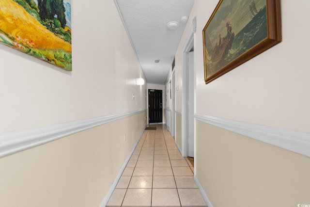 hall featuring a textured ceiling, baseboards, and light tile patterned floors