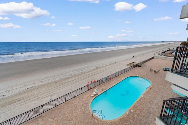 pool with a water view, fence, and a view of the beach