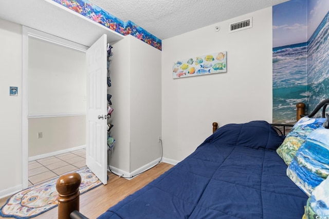 bedroom with a textured ceiling, wood finished floors, visible vents, and baseboards