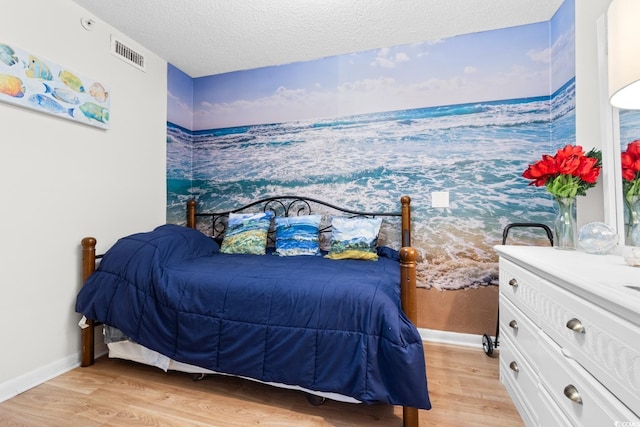 bedroom with baseboards, visible vents, light wood-style flooring, and a textured ceiling