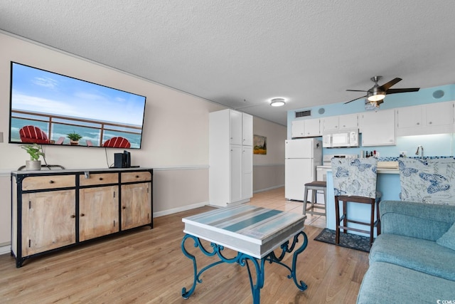 living room featuring a textured ceiling, ceiling fan, visible vents, and light wood-style flooring