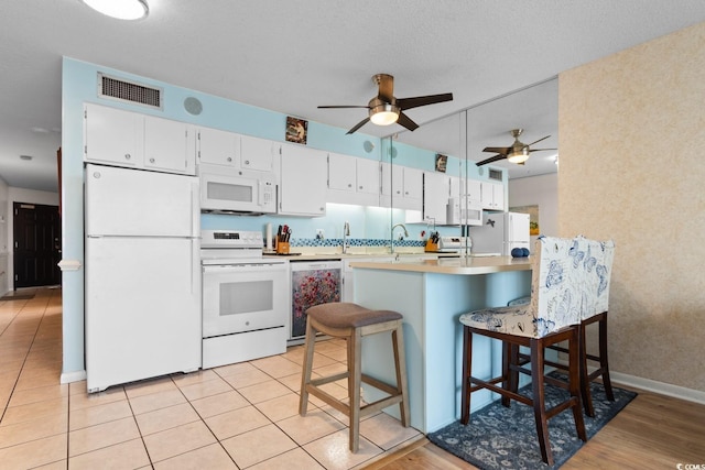 kitchen with a peninsula, white appliances, a sink, visible vents, and a kitchen bar