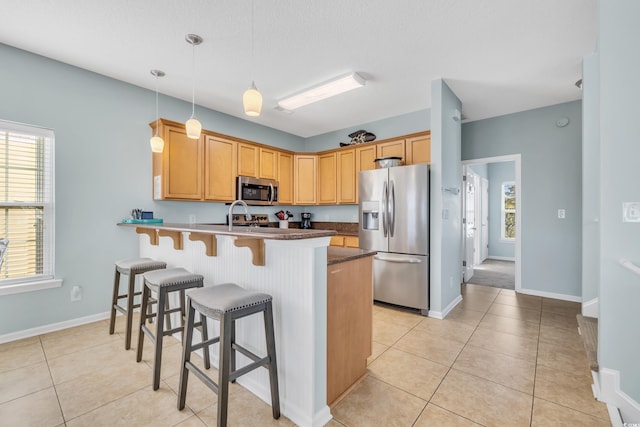 kitchen with light tile patterned floors, a peninsula, a kitchen breakfast bar, hanging light fixtures, and appliances with stainless steel finishes